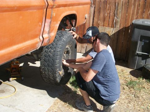 1969 Ford F-250 - Two men work on the wheel of an orange pickup truck, which appears to be from the early 1970s.