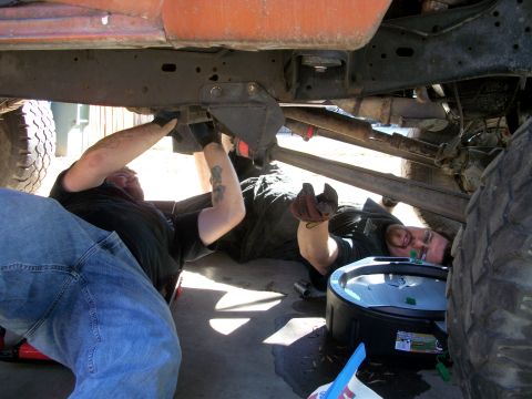 1969 Ford F-250 - Two individuals are shown performing maintenance on the underside of a vehicle, with tools and a drain pan nearby.