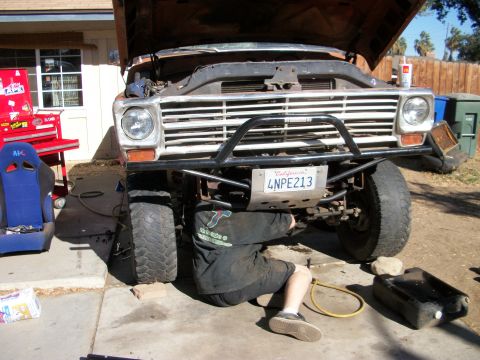 1969 Ford F-250 - A person works on the underside of a vintage Ford truck, with the hood open and tools nearby.