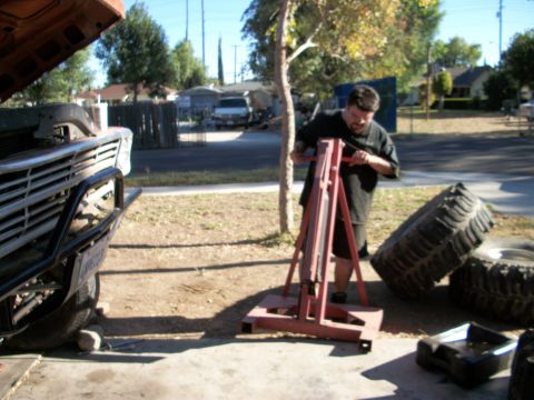 1969 Ford F-250 - A man is working on a truck with the hood open, using an engine hoist. A large tire lies nearby.