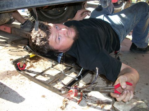 1969 Ford F-250 - A mechanic works on the underside of a vehicle, lying on a creeper.