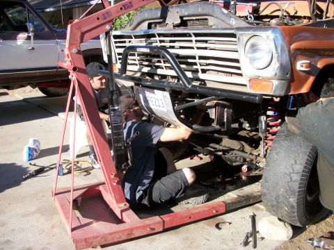 1969 Ford F-250 - Mechanics work on the front suspension of a truck, aided by an engine hoist. The license plate reads PE213.