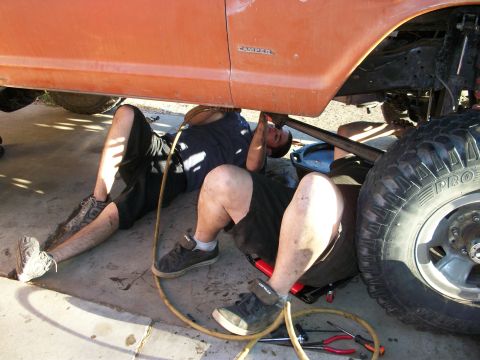 1969 Ford F-250 - Two mechanics are working on the underside of an orange truck, one using a creeper.