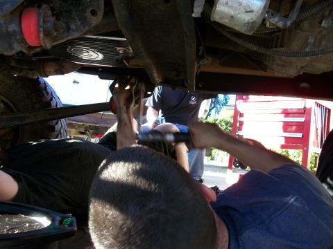 1969 Ford F-250 - Mechanics work on the underside of a vehicle, with tools and parts scattered around.