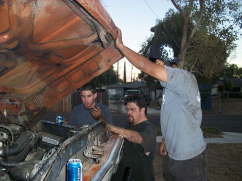 1969 Ford F-250 - Three men are gathered around the open hood of a truck, appearing to work on the engine bay.