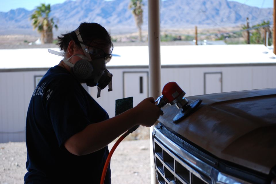 Person sanding hood of a 1980 Ford Bronco with a detail sander