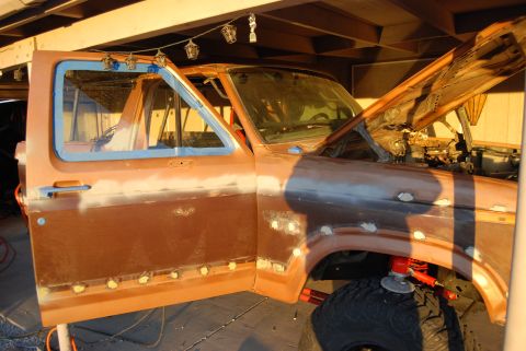 1982 Ford Bronco - Ford Bronco body in primer with door open and hood raised, showing bodywork in progress.