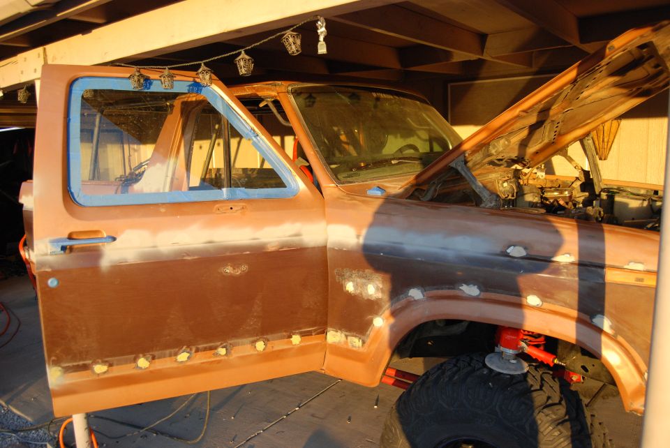 Ford Bronco body, driver's door open, hood up, undergoing bodywork. Primer and weld spots visible