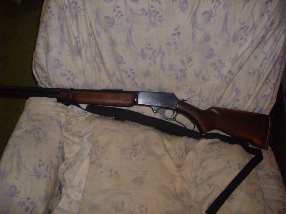 Wood-stocked lever-action rifle with black sling lying on a floral-print sheet