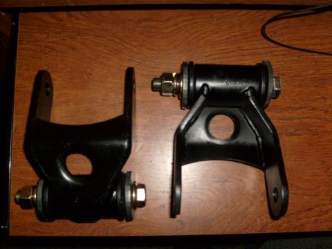 1986 Ford Bronco - Two black metal suspension components are shown on a wooden surface.