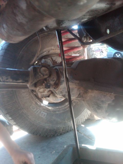 1982 Ford Bronco - Undercarriage of a vehicle, likely during an oil change, showing the drive shaft and tire.