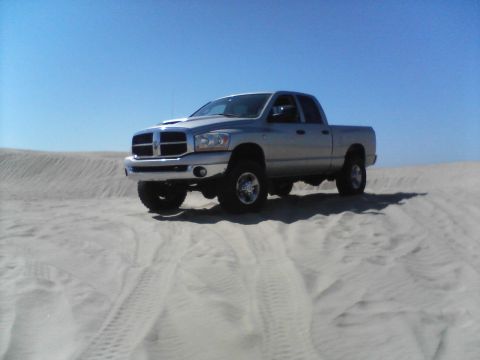 2006 Dodge 2500 - A silver 2006 Dodge 2500 pickup truck drives on sand dunes under a clear blue sky.