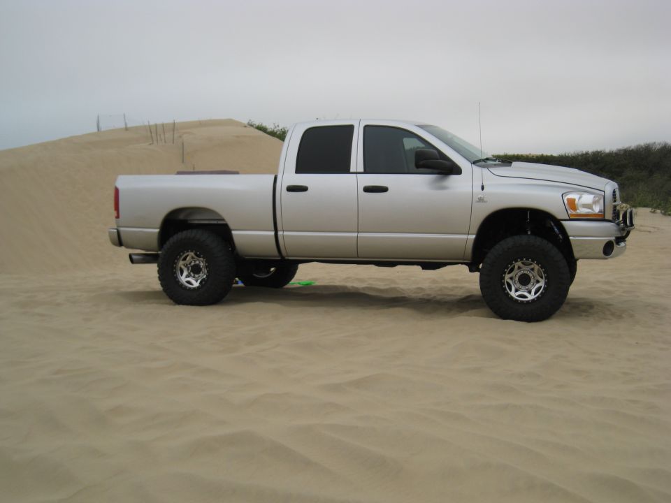 Silver Dodge 2500 pickup truck with lifted suspension and large tires parked on a sand dune