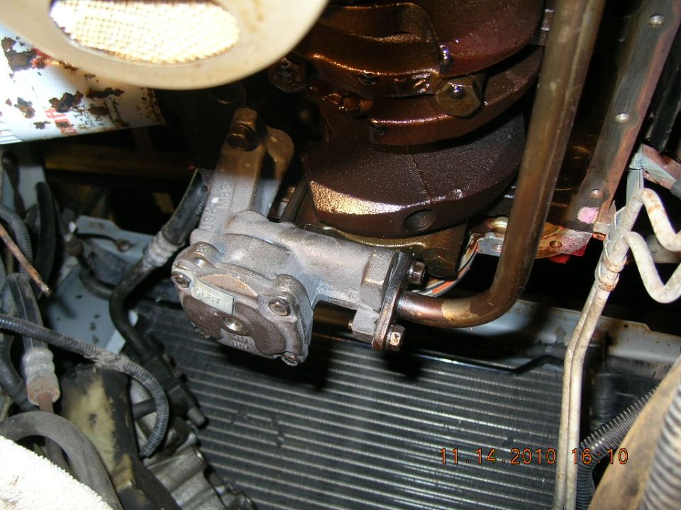 Close-up of a power steering pump mounted to an engine block, with hoses and a radiator visible