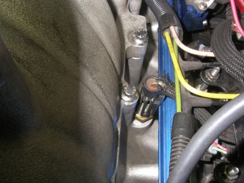 1990 Ford Bronco - Close-up inside an engine bay showing a blue-painted intake manifold and fuel rail with a small two-pin sensor connector unplugged and hang…