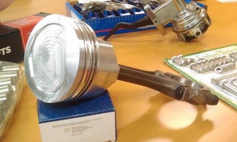 1973 Ford Ranchero - A close-up view of a piston and connecting rod assembly, likely for an engine rebuild, with other engine parts visible on a wooden surface.
