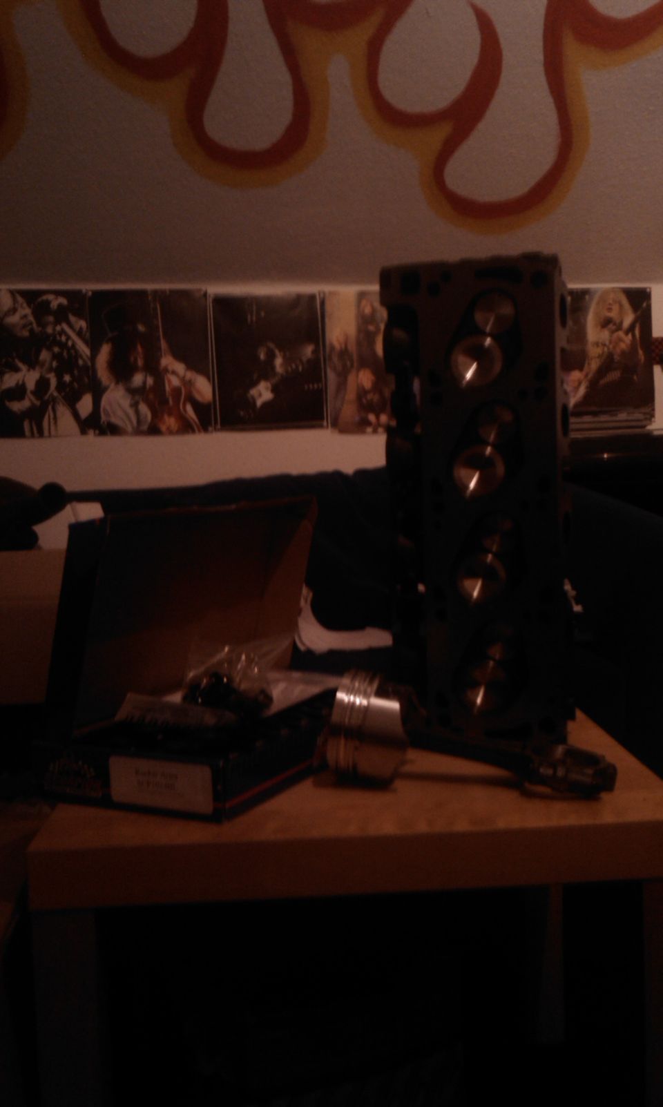 Engine cylinder head and piston on a wooden surface with posters on the wall