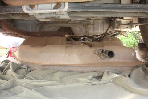 1990 Ford Taurus - The underside of a vehicle reveals a fuel tank, exhaust system components, and wiring harnesses.