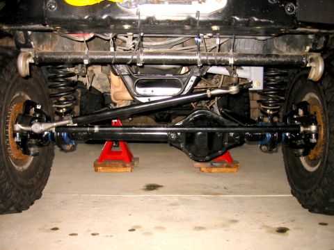 1985 Ford Bronco - The underside of a vehicle is visible, supported by red jack stands, revealing its suspension and steering systems.