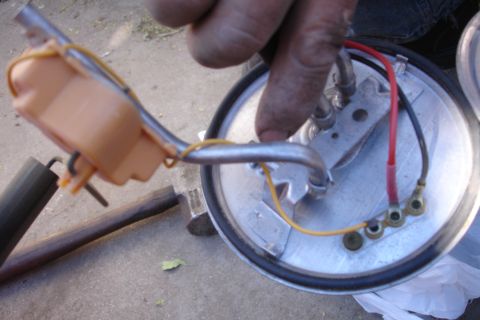 1990 Ford Taurus - Close-up of a fuel pump sending unit assembly removed from a fuel tank, showing the round metal mounting flange with red and yellow wiring,…
