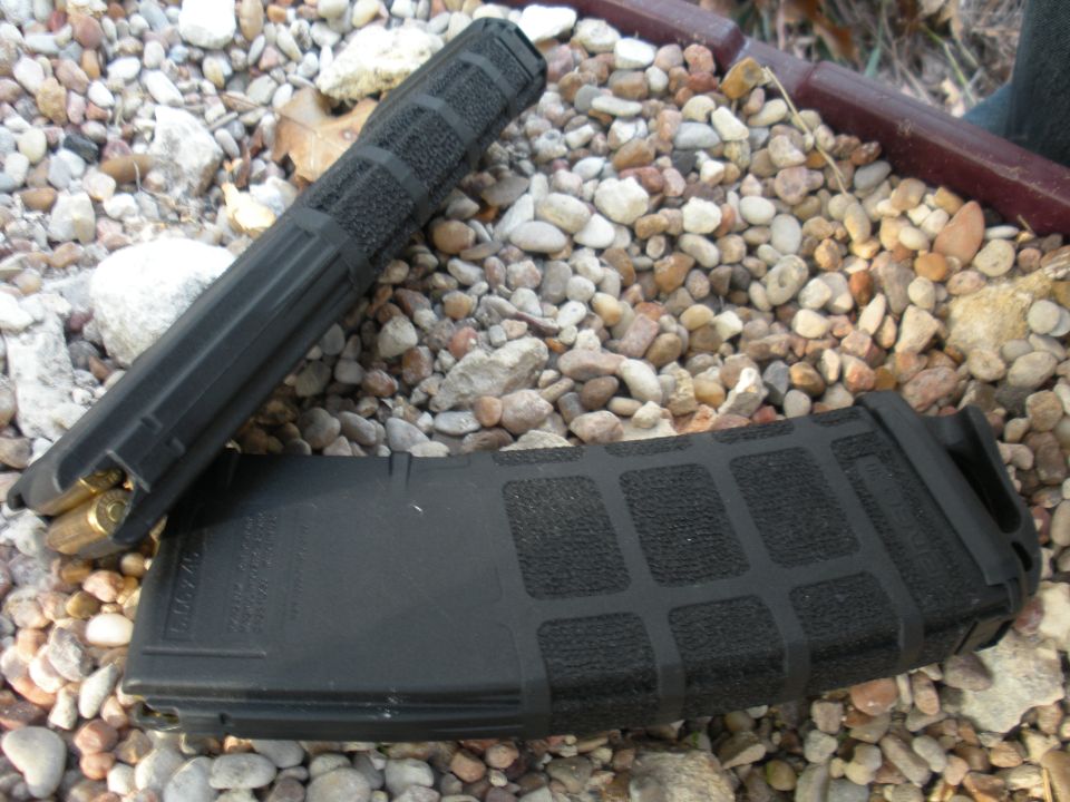 two black rifle magazines, one loaded with bullets, resting on gravel