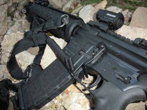 1996 Ford Bronco - Close-up of an assault rifle with a mounted optic and sling, placed on a rocky surface.