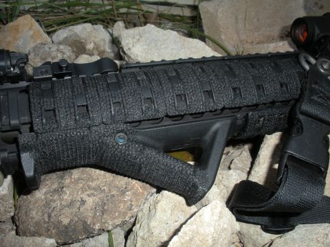 1996 Ford Bronco - Close-up of an AR-15 rifle's foregrip and vertical accessory, set against a rocky background.