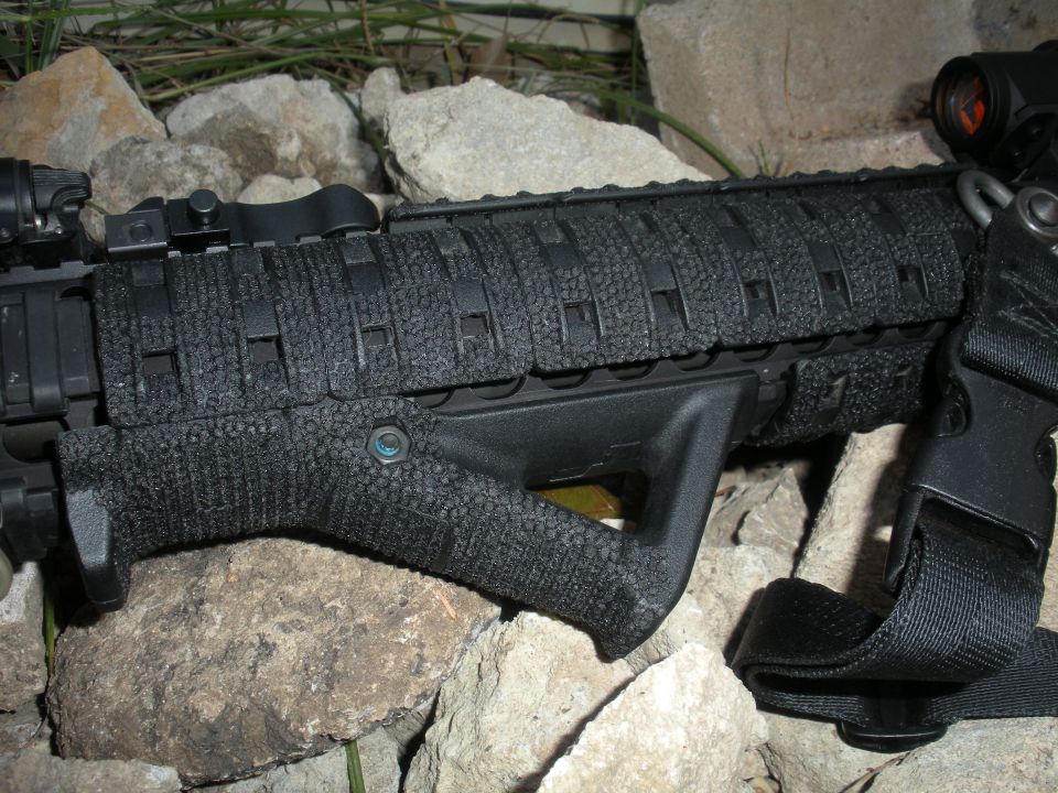 AR-15 rifle foregrip with textured grip and vertical handle, resting on rocks