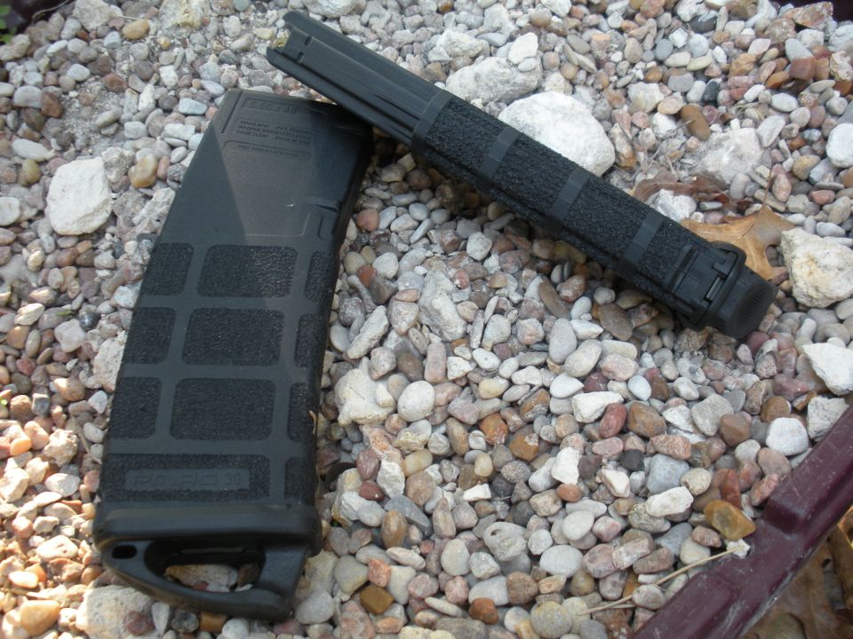 Two black rifle magazines and a foregrip lying on a bed of small rocks
