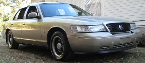 2000 Mercury Grand Marquis - A gold 2000 Mercury Grand Marquis is parked in front of a building with a black grille.