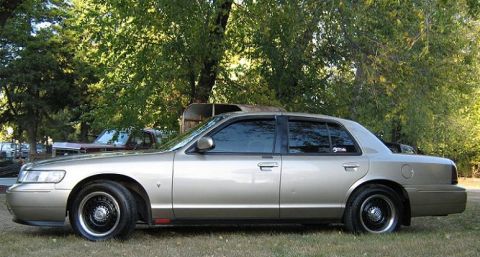 2000 Mercury Grand Marquis - A tan 2000 Mercury Grand Marquis sedan is parked outdoors with trees in the background and another vehicle visible behind it.