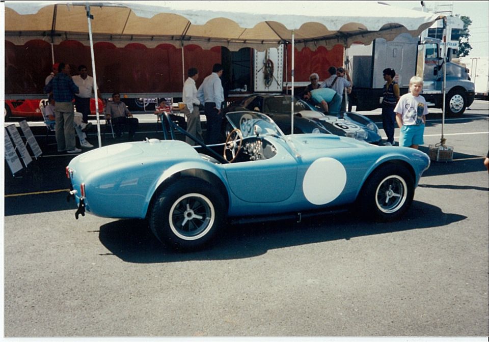 Light blue Shelby Cobra roadster with white roundel parked in a race paddock