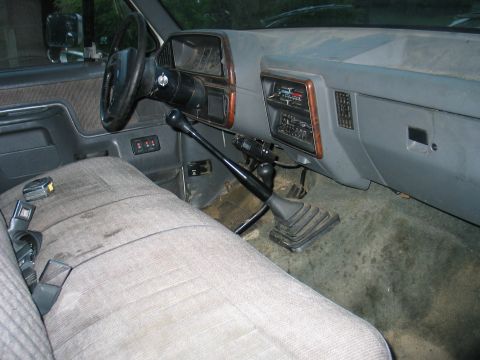 1984 Ford Bronco - Interior of a truck with a manual transmission and worn fabric seats.