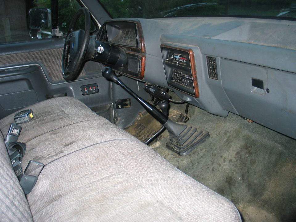 Interior view of a truck showing the driver's seat, dashboard, steering wheel, and manual shifter