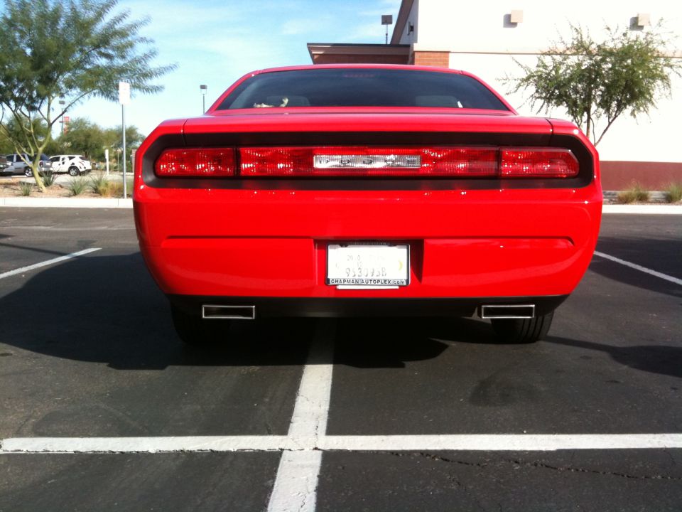 Rear view of red Dodge Challenger with dual exhaust tips and dealer paper tag