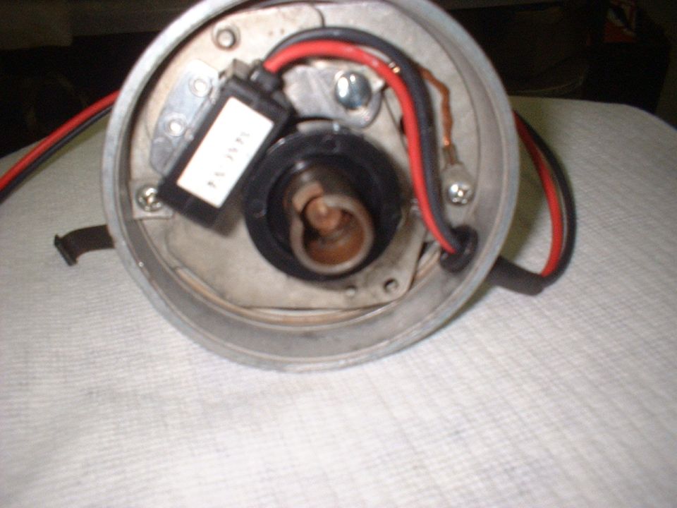 Close-up of an automotive distributor cap with red and black wires. A white label with text is visible