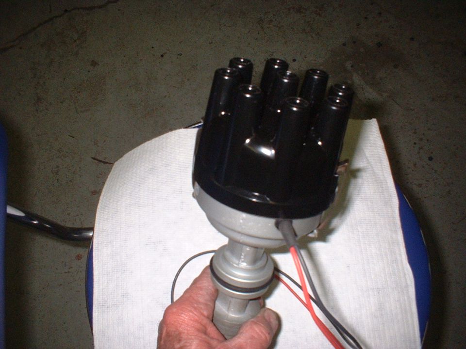 Hand holding a black automotive distributor with wires