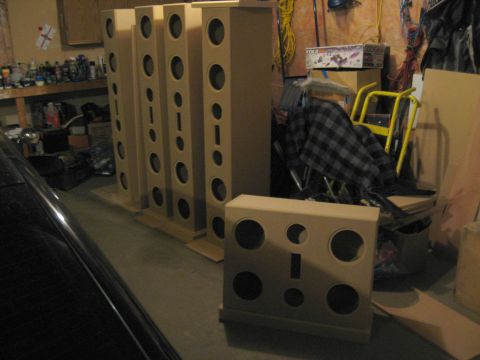 1987 Ford Bronco - Several unfinished speaker cabinets are arranged in a garage, with a black car partially visible on the left.