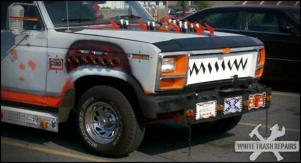 Modified pickup truck with shark teeth grille, red accents, and decorative plates on the bumper