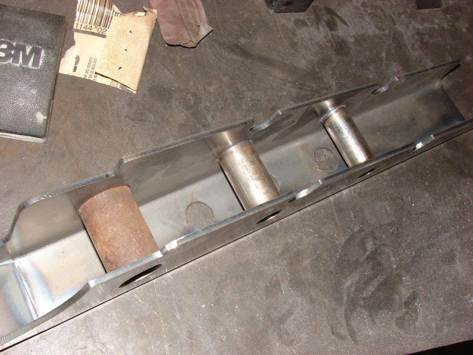Metal bracket with two silver pins and one rusty brown pin, on a workbench with sandpaper