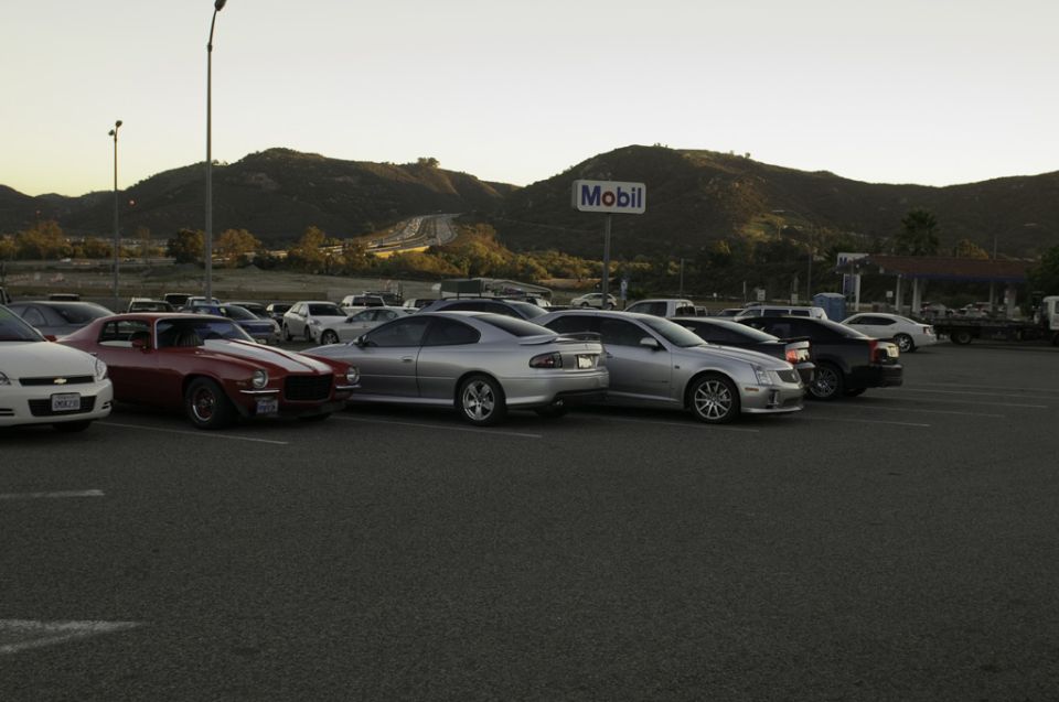 Cars parked in a lot with a Mobil sign and mountains in the background