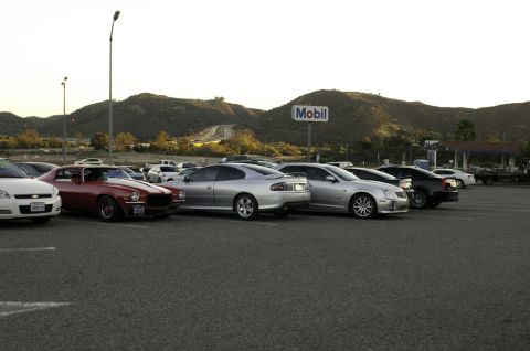 2006 Cadillac STS - Several cars are parked in a lot with a Mobil sign and hills in the background.