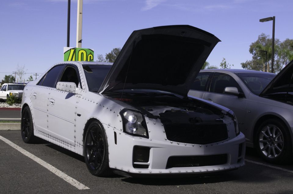 White car with exposed rivets, hood open, black wheels
