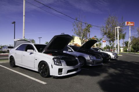 2006 Cadillac STS - Multiple Cadillac sedans, including a white 2006 STS, are parked with their hoods open under a blue sky.