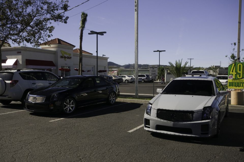 White Cadillac sedan parked in a lot, front view, with a black Cadillac sedan to its left