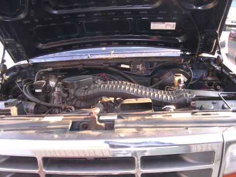 1995 Ford Bronco - The engine bay of a dark SUV is shown with the hood raised, revealing various mechanical components.