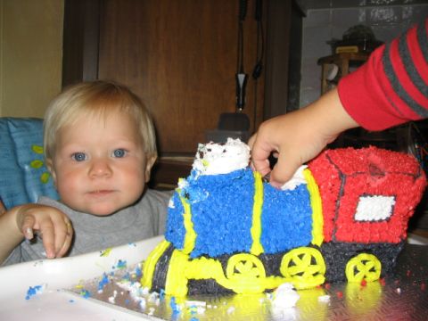 1986 Ford Bronco - A young child looks at a train-shaped birthday cake with a hand reaching to take a piece.