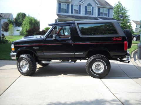 1995 Ford Bronco - Side view of a black Ford Bronco with aftermarket wheels and tires parked on a driveway.