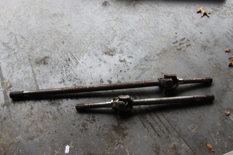 Two rusty drive shafts with universal joints on a concrete floor