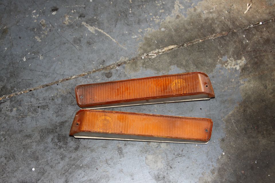 Two amber marker lights with ribbed lenses and chrome trim, lying on a concrete floor